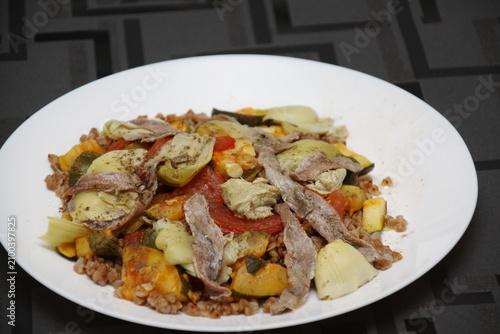 Appetizer, side salad with buckwheat, artichokes, tomatoes, zucchini, anchovies, olive oil, basil, herbs.