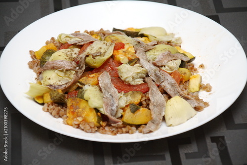 Appetizer, side salad with buckwheat, artichokes, tomatoes, zucchini, anchovies, olive oil, basil, herbs.