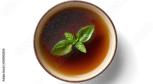 Overhead view of clear brown broth in a bowl, garnished with fresh green basil leaves
