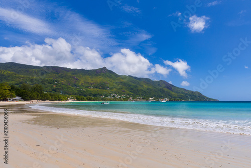 Landscape of Beau Vallon beach on a sunny summer day. Wet sandy shore is unde...