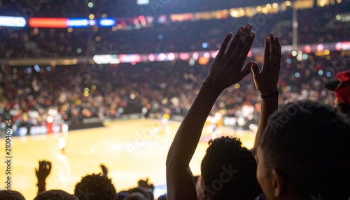 Excited fans cheering at a basketball game. Crowd raising hands in a packed sports arena.