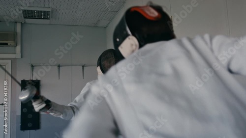Fencing sport. Sportsmen fencing training. Two swordsmen are doing sword moves. Fencer players in gym, indoor sports club. Two athletes practice epee, uniforms and masks. Olympic combat sport.