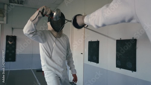 Fencing sport. Sportsmen fencing training. Two swordsmen are doing sword moves. Fencer players in gym, indoor sports club. Two athletes practice epee, uniforms and masks. Olympic combat sport.