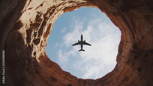 A low angle shot of an airplane flying through a natural rock arch under a blue sky