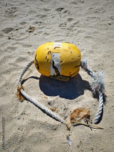Broken yellow buoy and frayed rope abandoned on a sandy beach