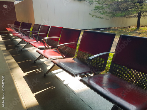 A row of empty waiting chairs illuminated by natural sunlight in a modern outdoor corridor.