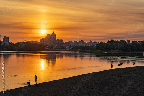 Beautiful golden sunset over Dnieper river with people silhouettes on the beach and Kyiv city skyline