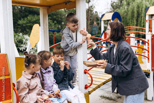 фотографія Smiling happy woman teacher sharing cookies with children at playground