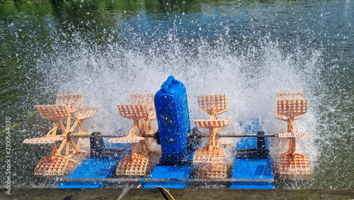 Floating paddle wheel aerator spraying water on a lake surface. Close up outdoor photography of pond aeration equipment
