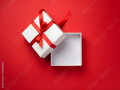 Open white gift box with red ribbon on red background for surprise and celebration