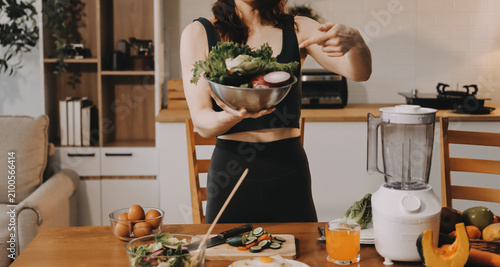 Woman preparing green smoothie in bright kitchen with fresh fruits and vegetables, healthy eating lifestyle moment in natural daylight