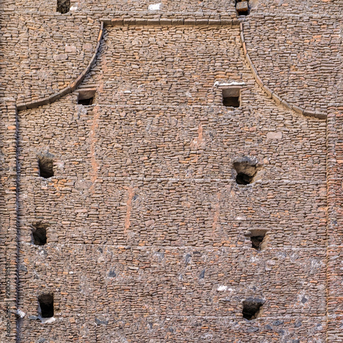 A shot of an ancient church wall in Catania Sicily, built entirely from reclaimed stones bricks and lava stone The masonry, showing scaffolding holes and the reconstruction following past earthquakes.