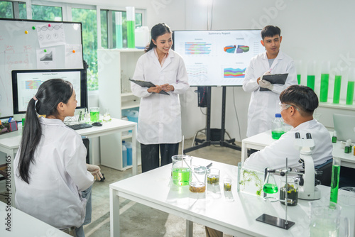 Laboratory student scientist chemistry experiment classroom beaker microscope group in white coat discuss green liquid research during science lesson with chart display and glassware