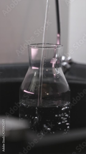 Fresh water pouring from tap into reusable sports bottle vertical