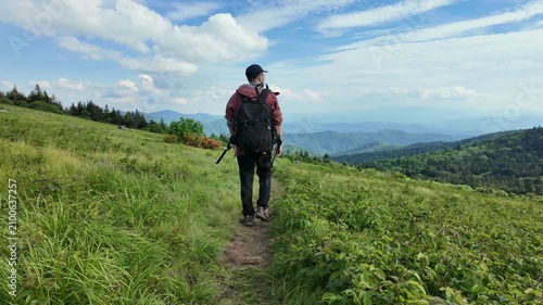 Hiker with a backpack walking through a green meadow at Roan Mountain North Carolina, surrounded by expansive Appalachian mountain scenery