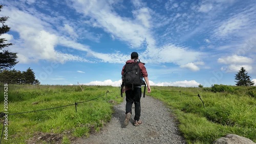 Hiker walking across Round Bald at Roan Mountain with open mountain views and clouds in the distance