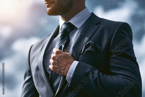 Man in a sharp suit adjusting his tie with a confident expression and a hint of sunlight