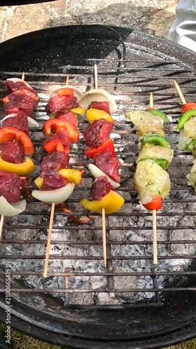 Skewers cook over a charcoal BBQ while the cook closes the lid.