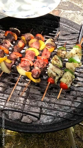Lifting grilled fish skewers off the charcoal BBQ and serving them on a plate.