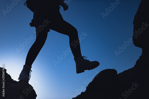 Hiker's silhouette stepping over a rock crevice, symbolizing progress, bravery, and the challenge of navigating difficult terrain during an outdoor trek