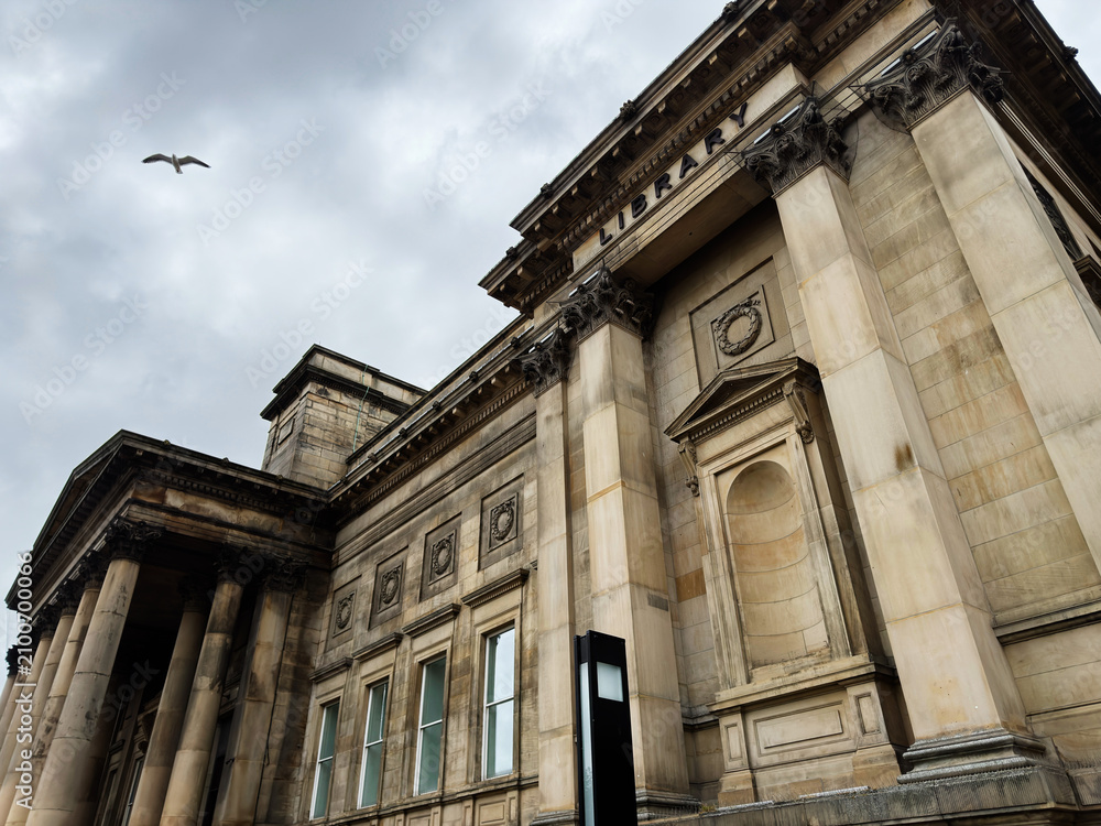 Obraz premium Neoclassical library building in Liverpool with grand stone columns and ornate façade under a cloudy sky with a seagull flying overhead