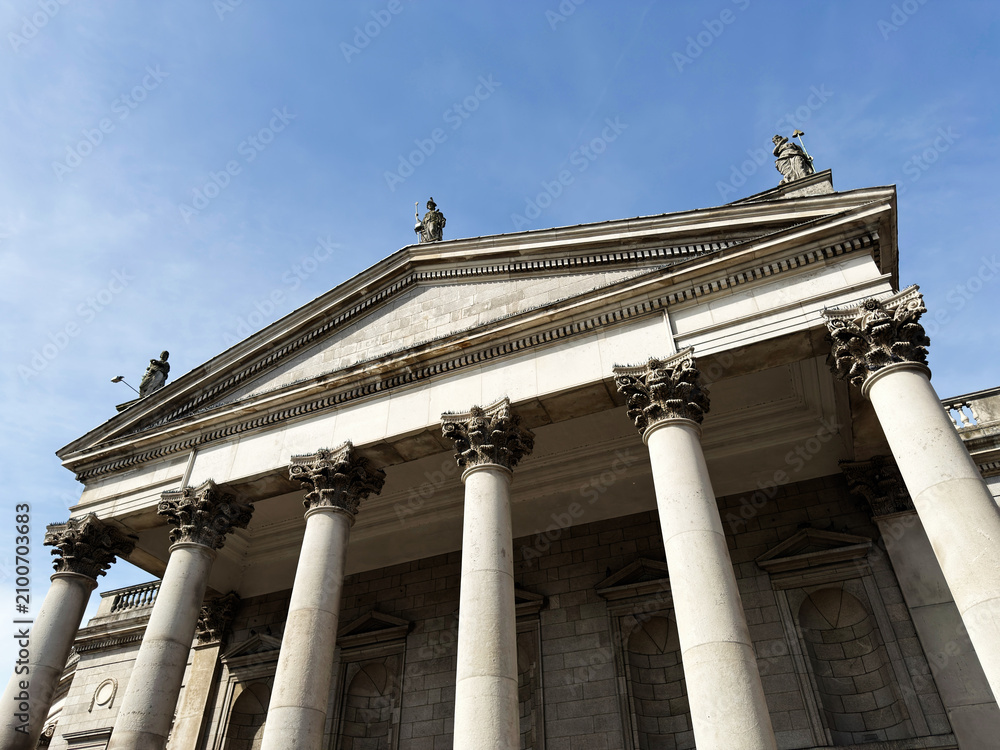 Obraz premium Neoclassical Bank of Ireland building facade with Corinthian columns and rooftop statues in Dublin, Ireland, classical architecture under a clear blue sky
