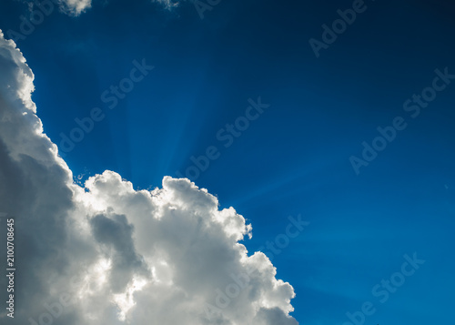 Dramatic blue sky with sun rays shining through fluffy white clouds