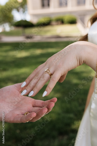 Close-up of bride reach her hands to grooms hand with diamond engagement ring and wedding band