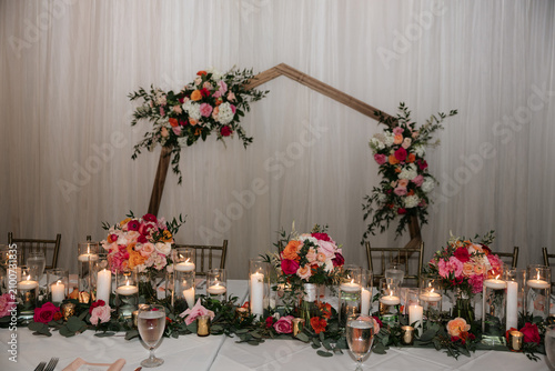 Modern geometric wooden wedding arch decorated with vibrant spring flowers
