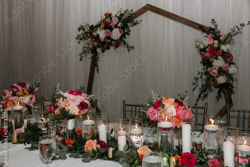 Modern geometric wooden wedding arch decorated with vibrant summer flowers behind head table