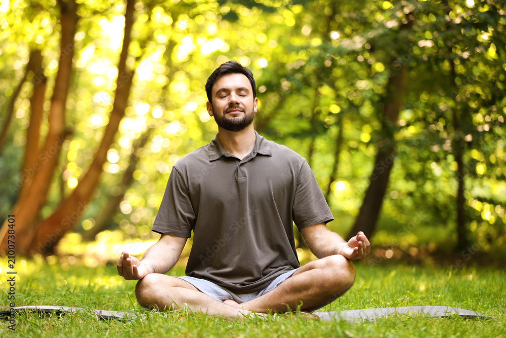Obraz premium Handsome man practicing yoga on mat in park