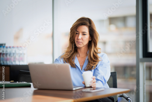 Canvas Print Confident middle-aged businesswoman using her laptop in a modern office