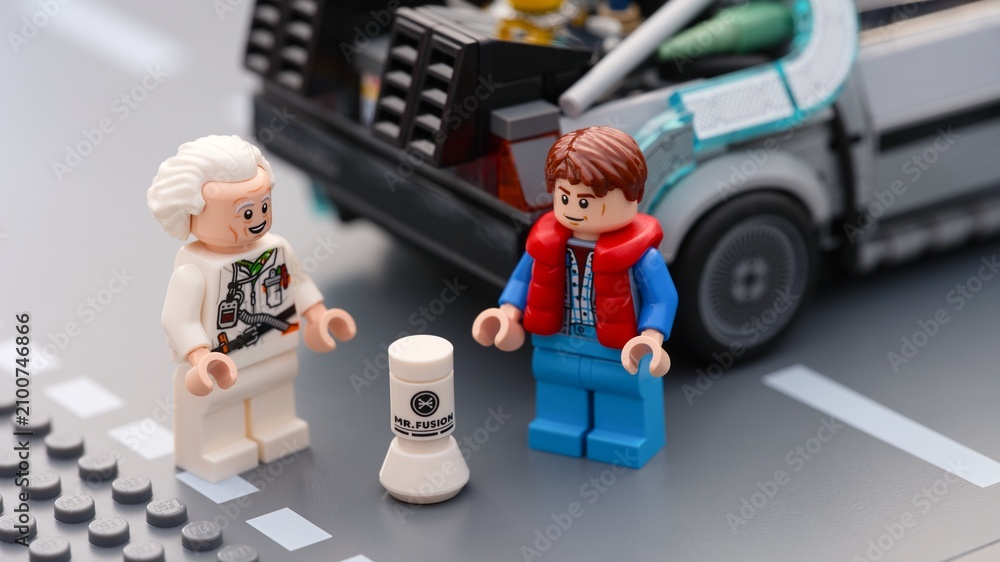Fototapeta premium Tambov, Russian Federation - July 12, 2026 Lego minifigures of Doc Brown and Marty McFly standing on a road next to the Mr. Fusion home energy reactor and the DeLorean time machine car.