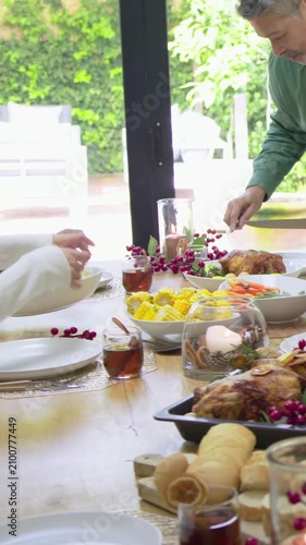 Vertical video: Reaching guests as host in green shirt carving roast at home table with fork, knife