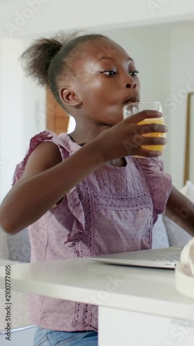 Vertical video: Glancing at laptop, girl in purple top sipping juice and typing work at home