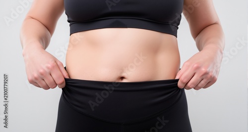 Close-up of a woman pulling her loose waistband to show weight loss results after a successful diet and exercise routine.
