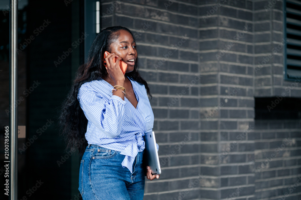 Fototapeta premium Black woman talking on phone carrying laptop