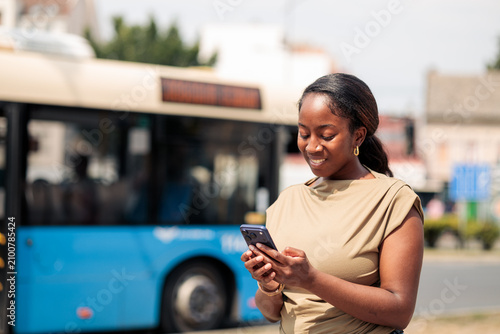Foto Young black woman messaging on smartphone at bus stop