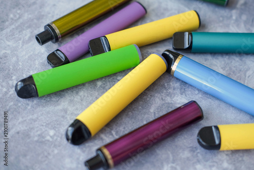 Disposable electronic cigarettes against a grey background. Concept of modern smoking, vaping, and nicotine.