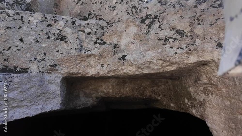 Salina, Malta - a young boy stands before a dark, rectangular entrance carved into weathered limestone rock, marking one of the ancient Paleo-Christian catacombs surrounded by layered stone blocks.