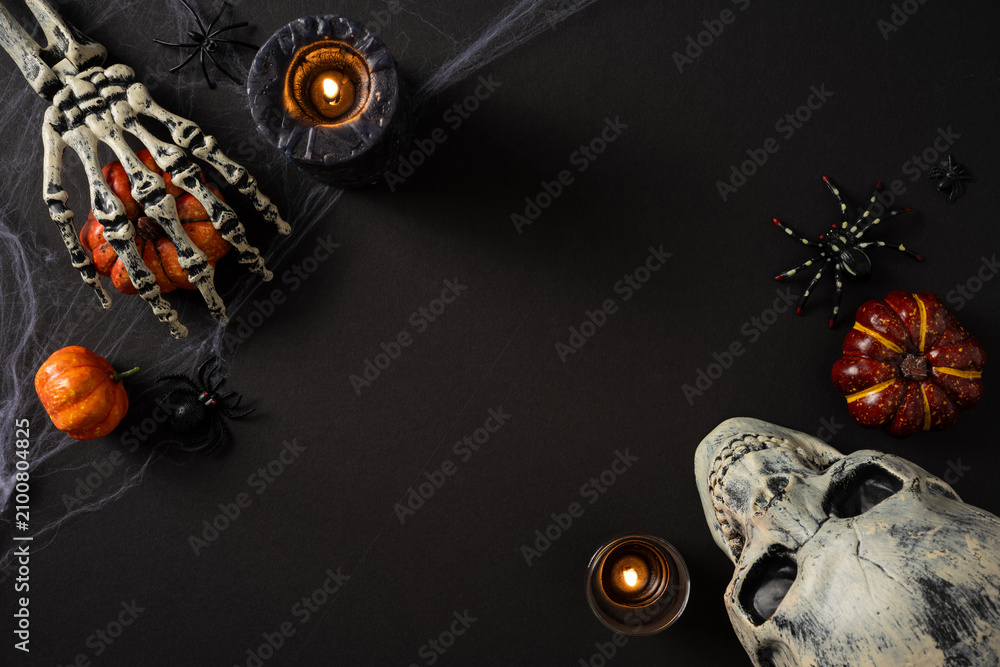 Obraz premium Happy Halloween spooky flat lay with skull, skeleton hand holding pumpkin, candles and spiders