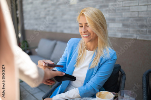 Woman making contactless payment using smartphone at cafe