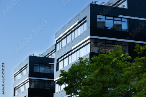 Modern commercial building with large glass windows and sleek black facade surrounded by green trees under a clear blue sky in an urban setting