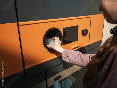 Young woman inserting plastic water bottle into reverse vending machine, eco recycling concept
