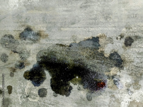 Close view of a large stain of black used oil over a rustic concrete floor