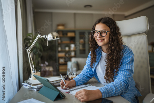 Teen girl studying homework at home desk smiling