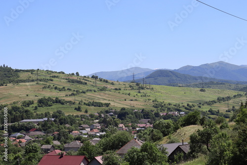 Mountain village surrounded by green hills beneath clear blue summer sky