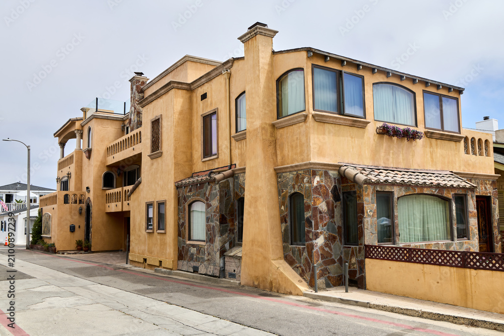 Fototapeta premium Mediterranean style luxury villa exterior with warm stucco facade, natural stone accents, terracotta roof tiles and elegant balconies on a coastal California street.