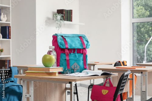 Colorful school backpack with books, apple, and water bottle on a classroom d...
