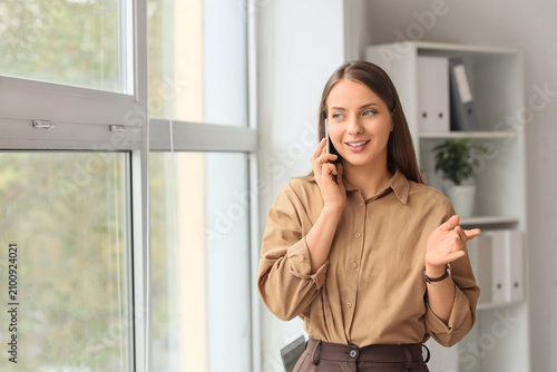 Young businesswoman talking by mobile phone near window in office